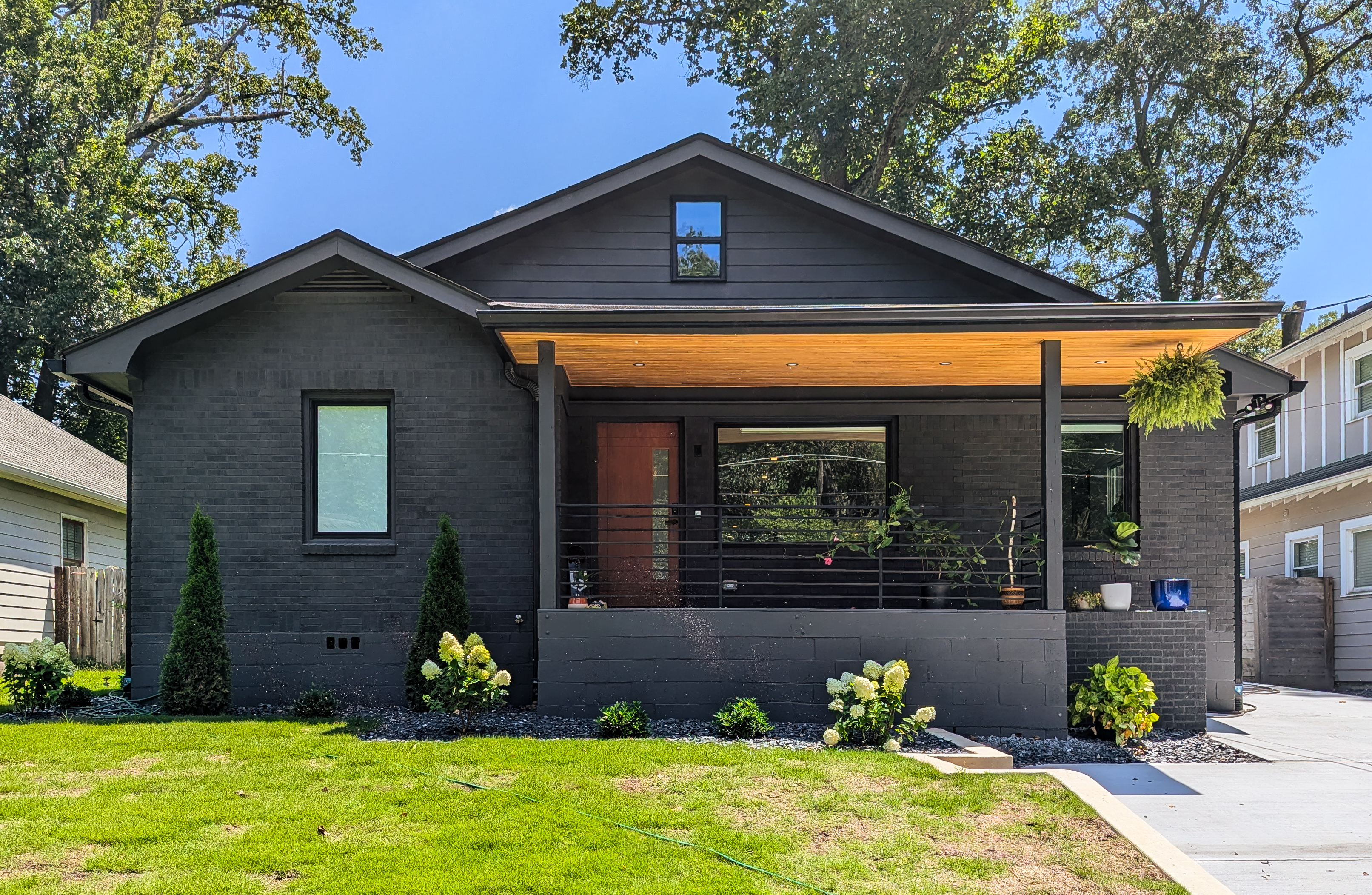 A modern black brick bungalow with warm wood porch ceiling